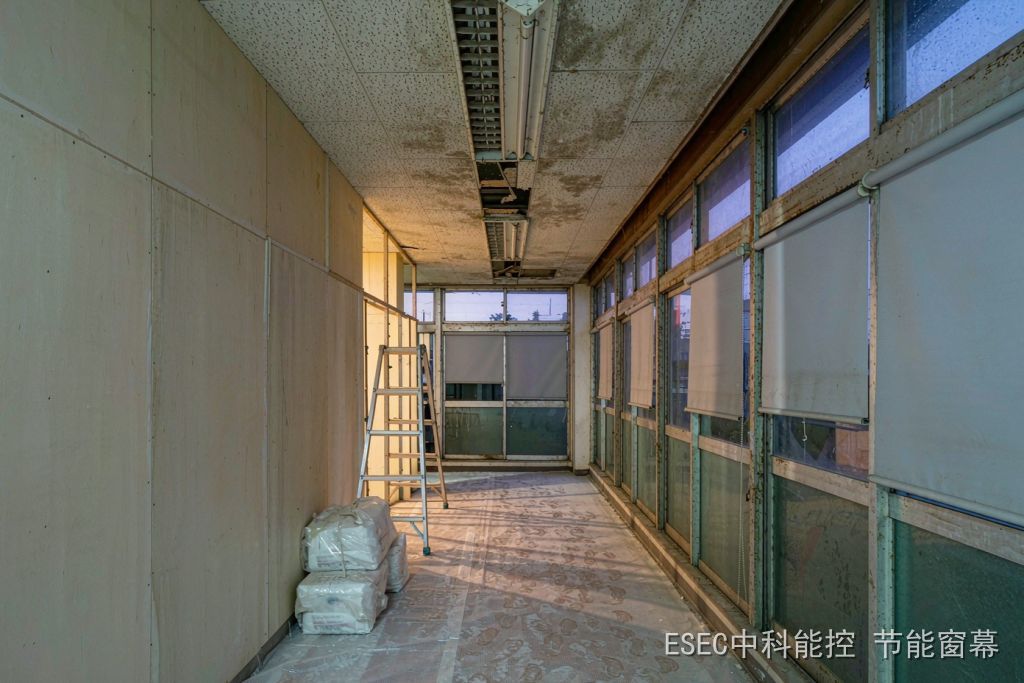 旧办公楼改造为长租公寓的走廊,左侧新砌隔墙、右侧保留的旧铝合金推拉窗与半降遮阳卷帘