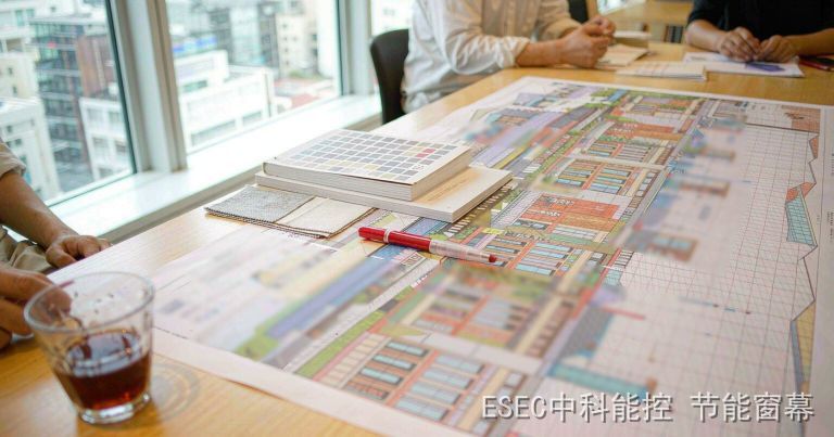 技术评审会议室长桌上摊开的建筑立面图纸、色卡与遮阳面料小样，红笔压在图上
